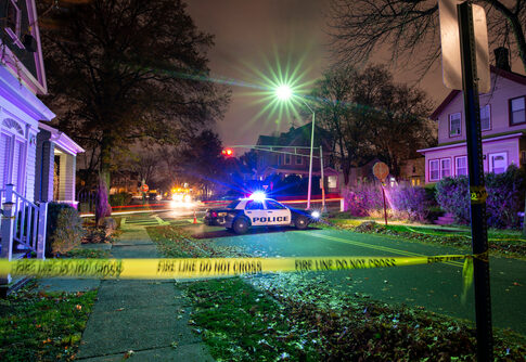 Police car with flashing lights at a crime scene surrounded by caution tape