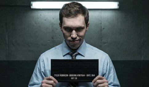 A man in a blue shirt holding a police mugshot board with his booking information