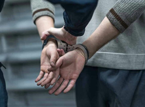 Person in handcuffs being detained by another person.