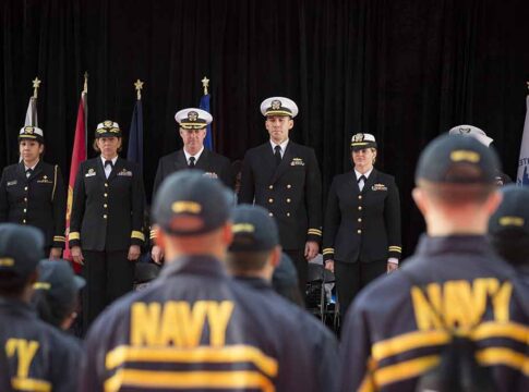 Navy officers stand at attention on stage during a ceremony