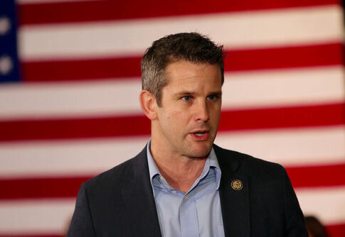 Man speaking in front of American flag backdrop.